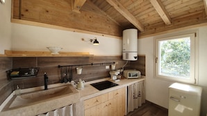 Cocina con armarios de madera, un lavamanos, estufa, tostadora y ventana con vistas a árboles.