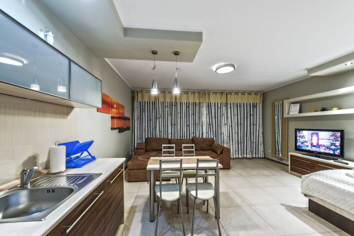 A modern living room with a sofa, TV, dining table, and kitchen area.