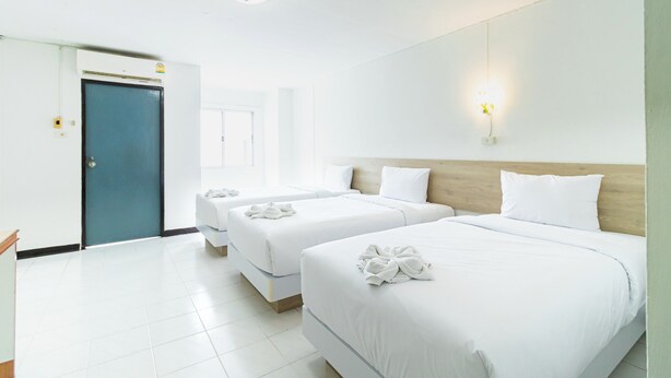 A hotel room with three beds, a wooden headboard, white bedding, and a blue door. - Boonchai Mansion (Hat Yai)