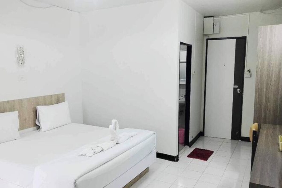 Una habitación de hotel con una cama, cabecera de madera, una puerta y un pequeño tapete rojo.