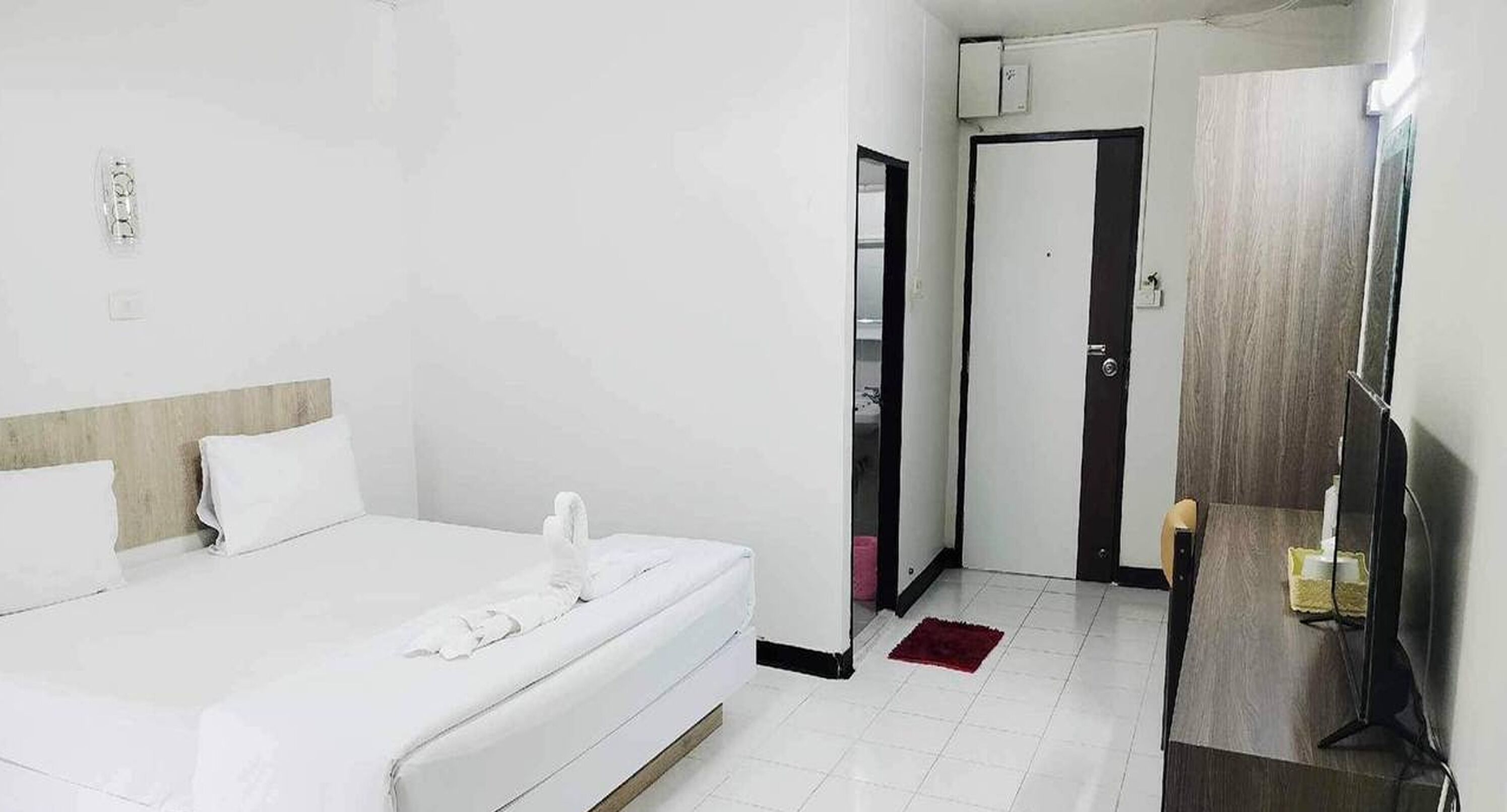 A hotel room with a bed, a desk, a chair, a TV, and a door.