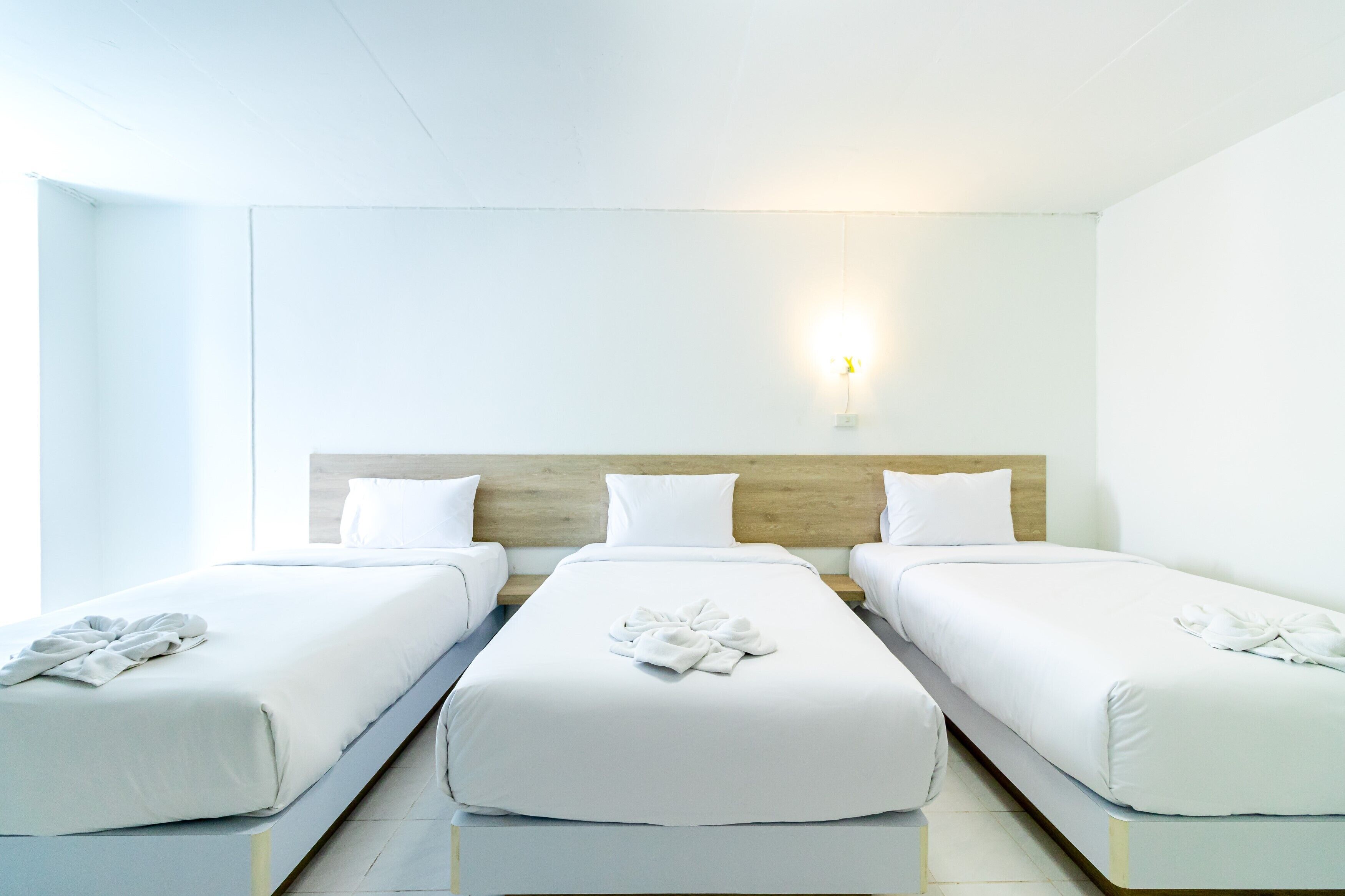 Ein Hotelzimmer mit drei Einzelbetten, jeweils mit einem ordentlich gefalteten Handtuch, weißer Bettwäsche und einem hölzernen Kopfteil.