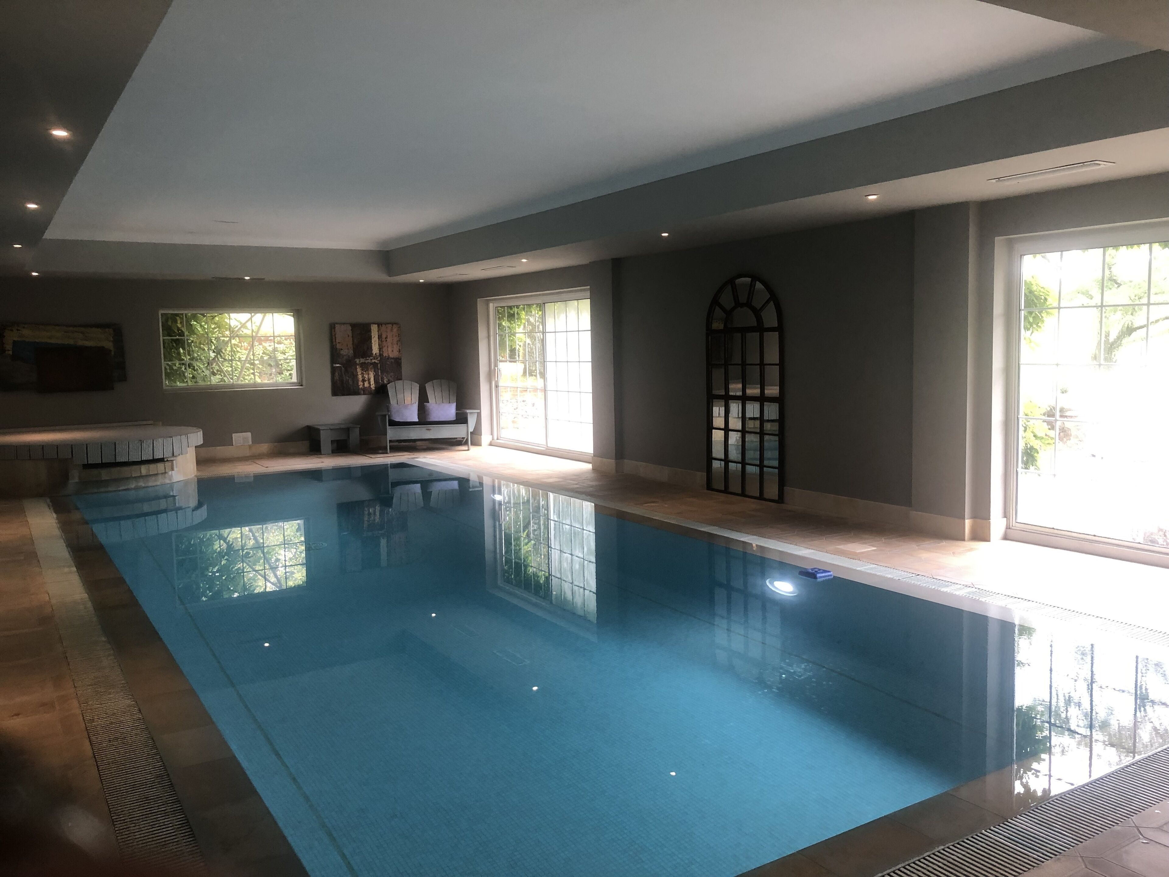 A swimming pool with a tiled floor, a bench, and two chairs.