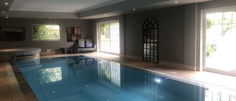 A swimming pool with a tiled floor, a bench, and two chairs.