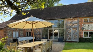 Une terrasse avec une table et des chaises, un grand parasol et un bâtiment en briques doté d’une porte en verre.