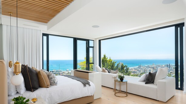 A modern bedroom with a large bed, a sofa, and a view of the city and sea. - Coeur De Lion 5 (Cape Town)