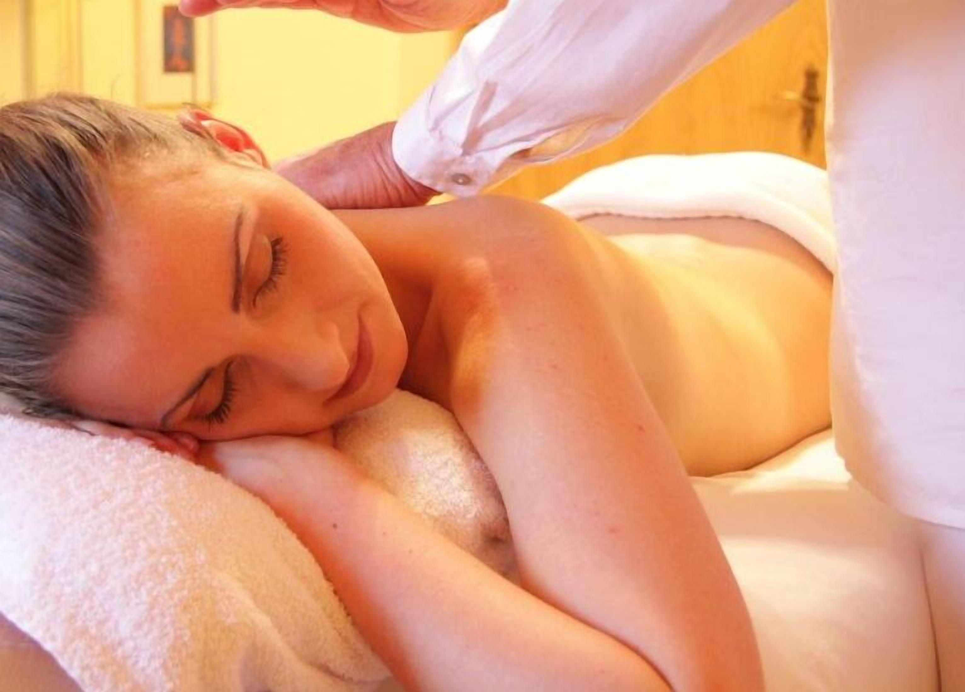 A person receiving a massage in a room with a bed and a white blanket.