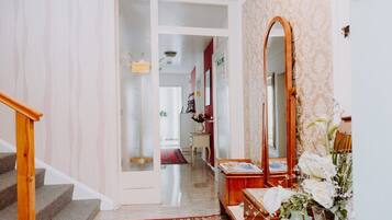 Un escalier menant à un couloir où se trouvent un miroir, un vase de fleurs et une porte avec une pancarte.
