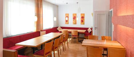 Un comedor con mesas y sillas de madera, un banco tapizado de rojo y obras de arte en las paredes.