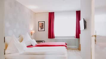 Habitación de hotel con cama, radiador, televisor montado en la pared y ventana con cortinas rojas.