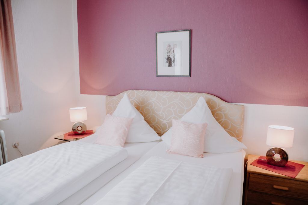 A neatly made bed with white linens, two bedside tables with lamps, and a framed picture on the wall.