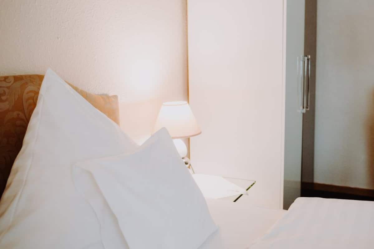 A hotel room with a bed, pillows, a lamp, and a door.