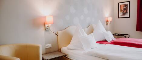 A hotel room with a bed, a chair, a nightstand, and wall-mounted lamps.