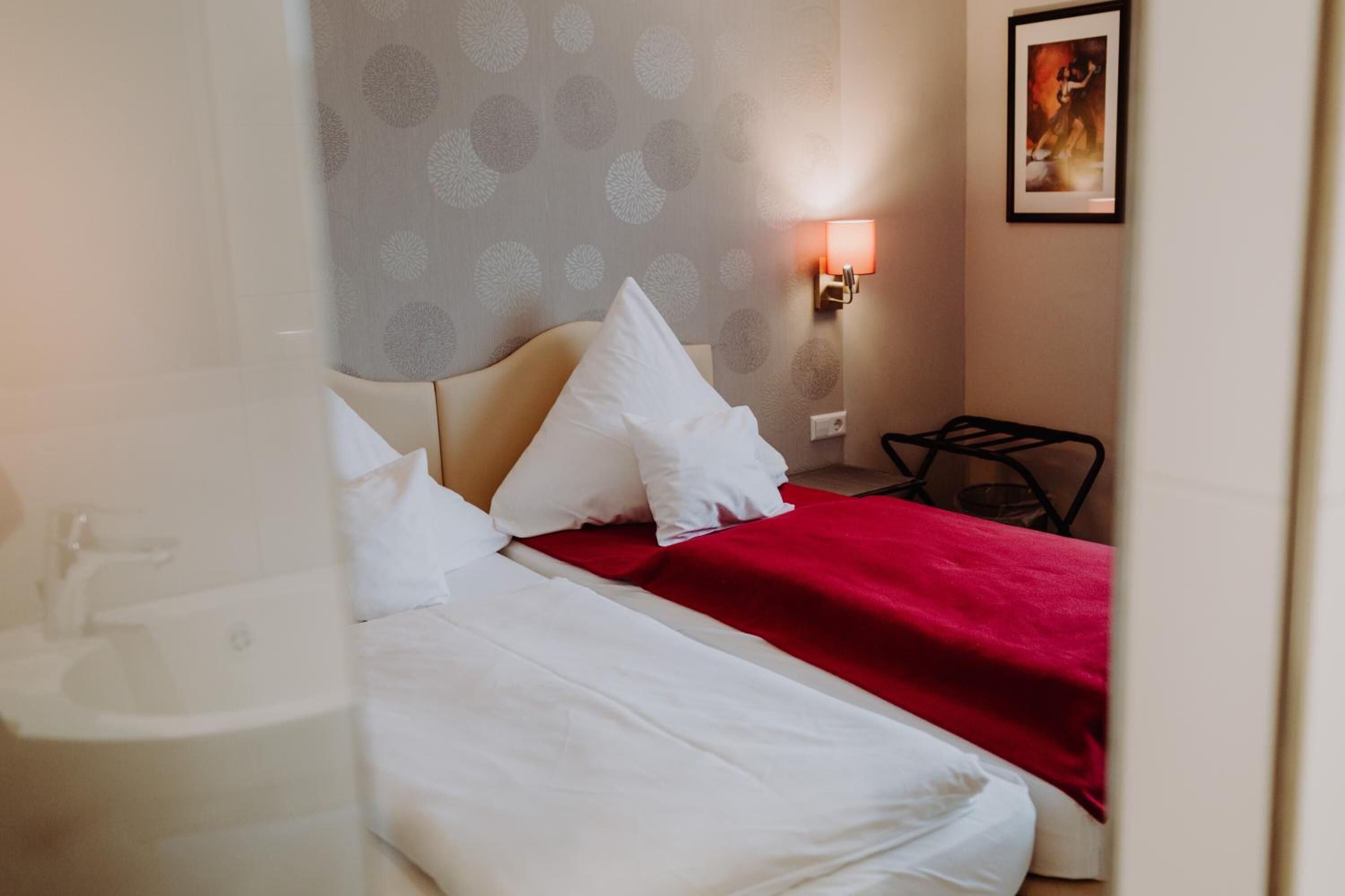 Een hotelkamer met twee bedden, een rode sprei, witte kussens, een hoofdeinde, een wandlamp en een lijst met een afbeelding.