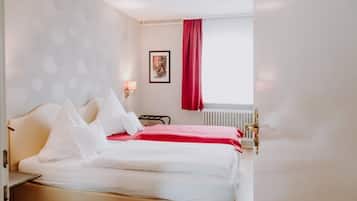 Una habitación de hotel con una cama, una cortina roja, un radiador y un cuadro en la pared.