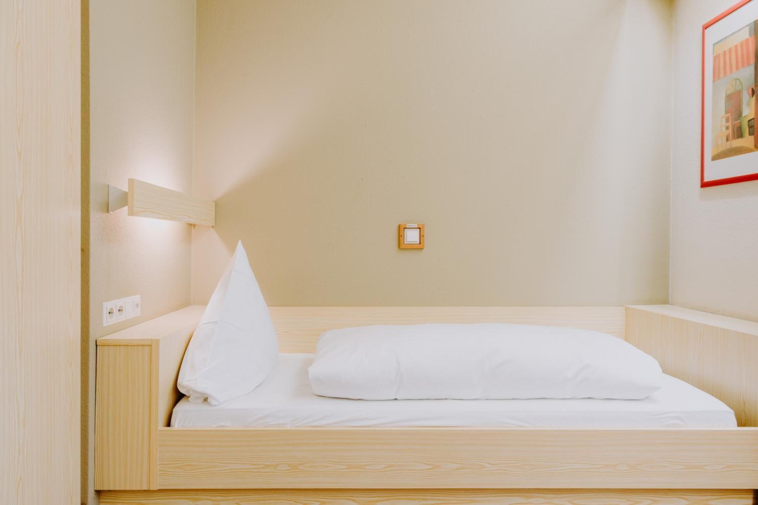 A single bed with white bedding in a room with light wooden walls and a small picture frame on the wall.