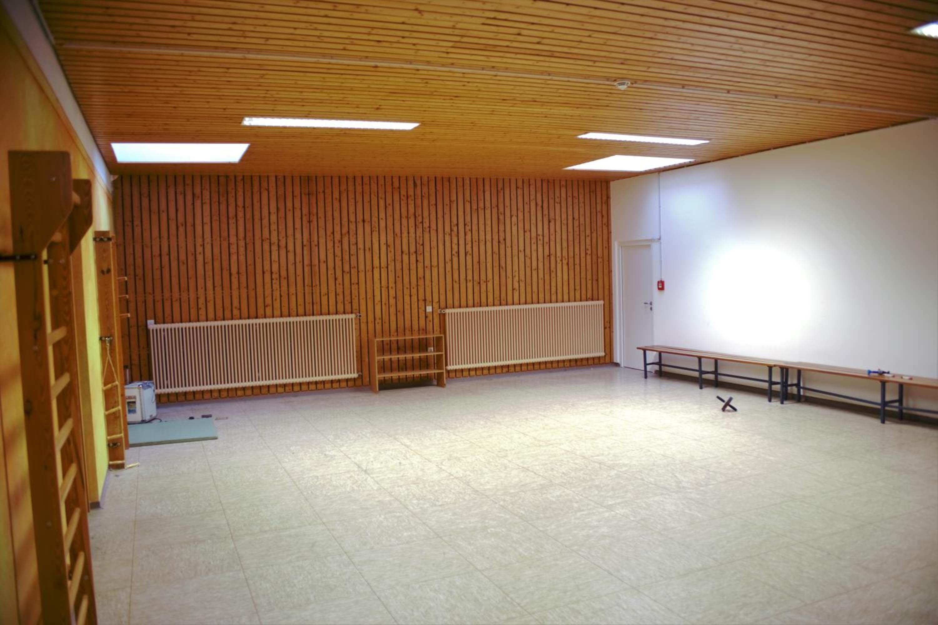 A spacious room with a high ceiling, wooden panel walls, a radiator, and a bench along one wall.