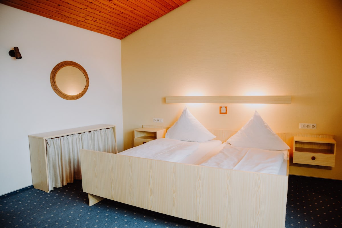 A neatly arranged hotel room with a wooden bed, bedside tables, a mirror, and a ceiling light fixture.