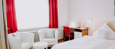 Une chambre d’hôtel avec un lit, un bureau, une chaise, une petite table et un radiateur.