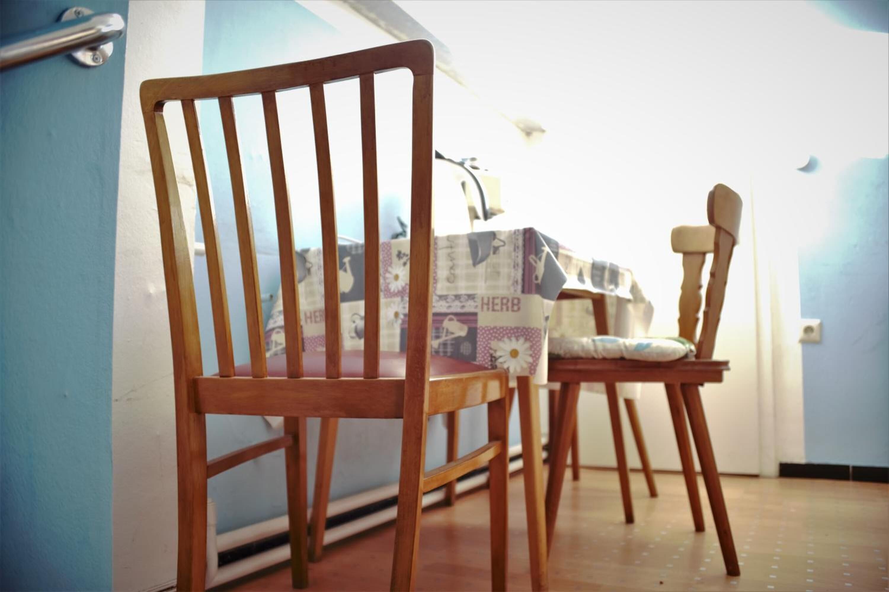 Een kamer met twee houten stoelen en een tafel met een tafelkleed met bloemen.