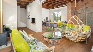 A modern living room with a glass coffee table, hanging wicker chair, and a dining area with a brick wall and large window. - Pine Road 26 (Cape Town)