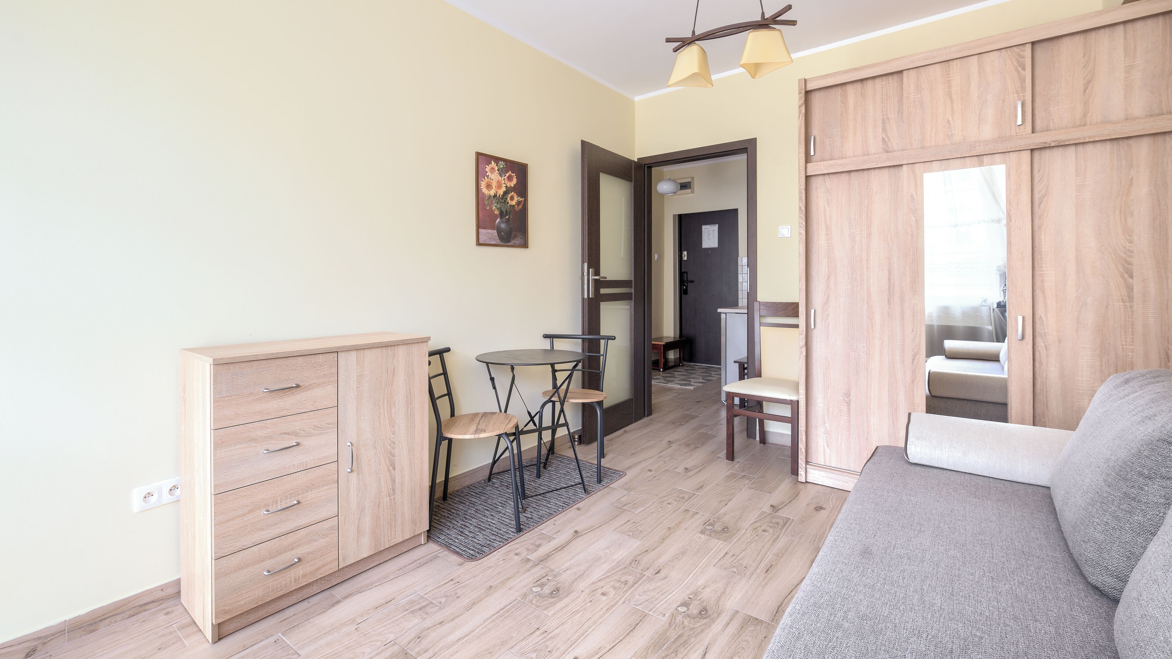 A compact living space with a sofa, a dining table with chairs, a cabinet, and a mirror.