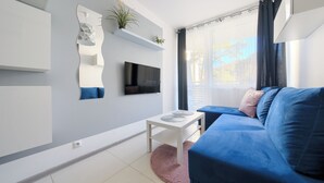 A modern living room with a blue sofa, a flat-screen TV, a white coffee table, and a pink rug. - Apartamenty Sun & Snow Nowa Slavia (Miedzyzdroje)