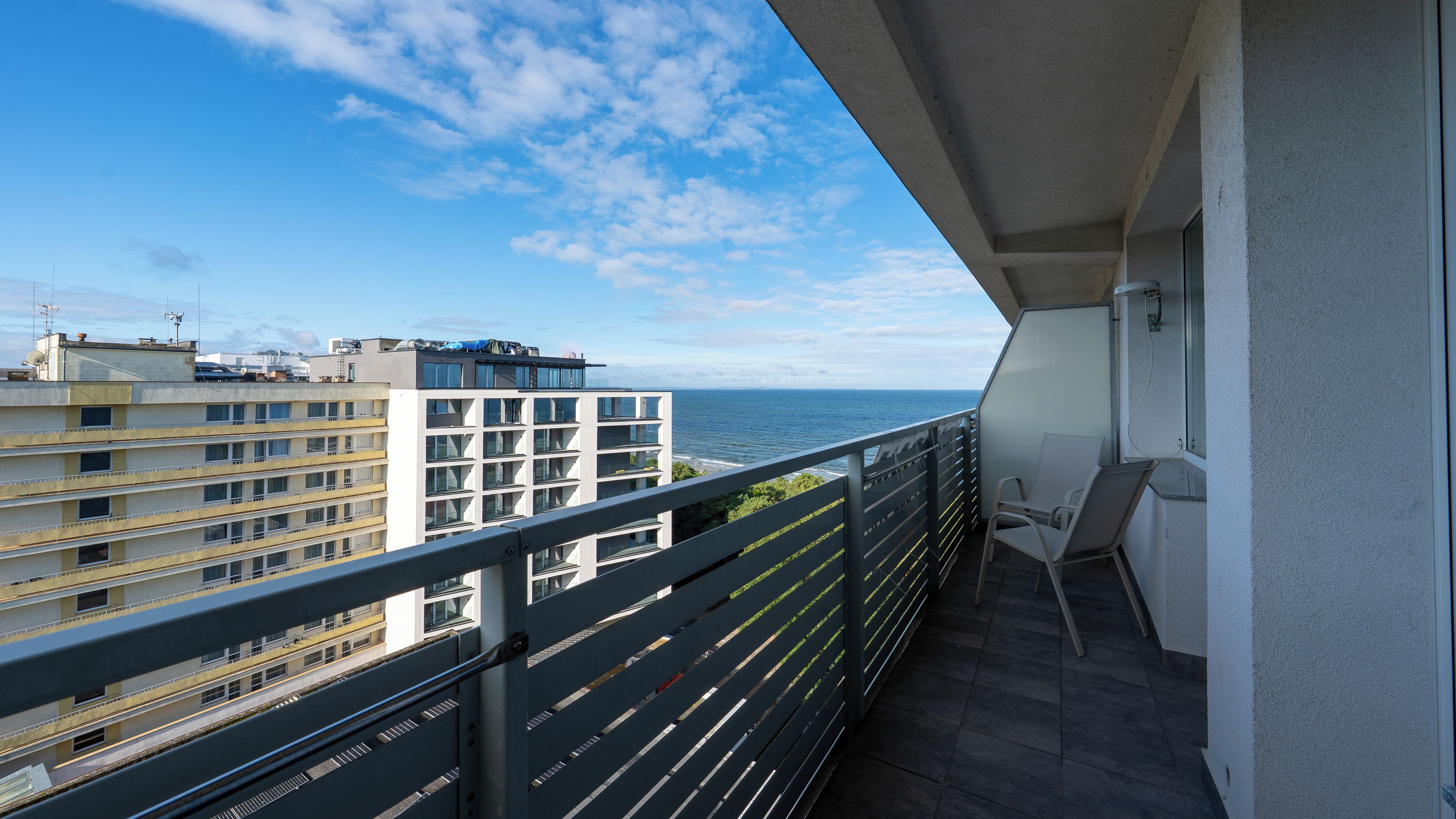 A balcony with a view of the sea, a chair, and a railing.