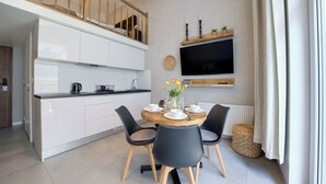 A modern kitchen with white cabinets, a dining table with black chairs, and a mounted TV. - Apartamenty Sun & Snow Nowa Slavia (Miedzyzdroje)