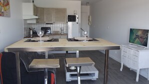 Una cocina compacta con microondas, tostadora y lavamanos. Hay dos taburetes y una mesita. Un televisor está montado en la pared.