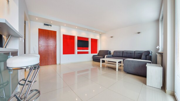 A modern living room with a grey sofa, a white coffee table, and a red accent wall.