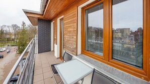A balcony with a table and chairs, large windows, and a view of a parking area and buildings.