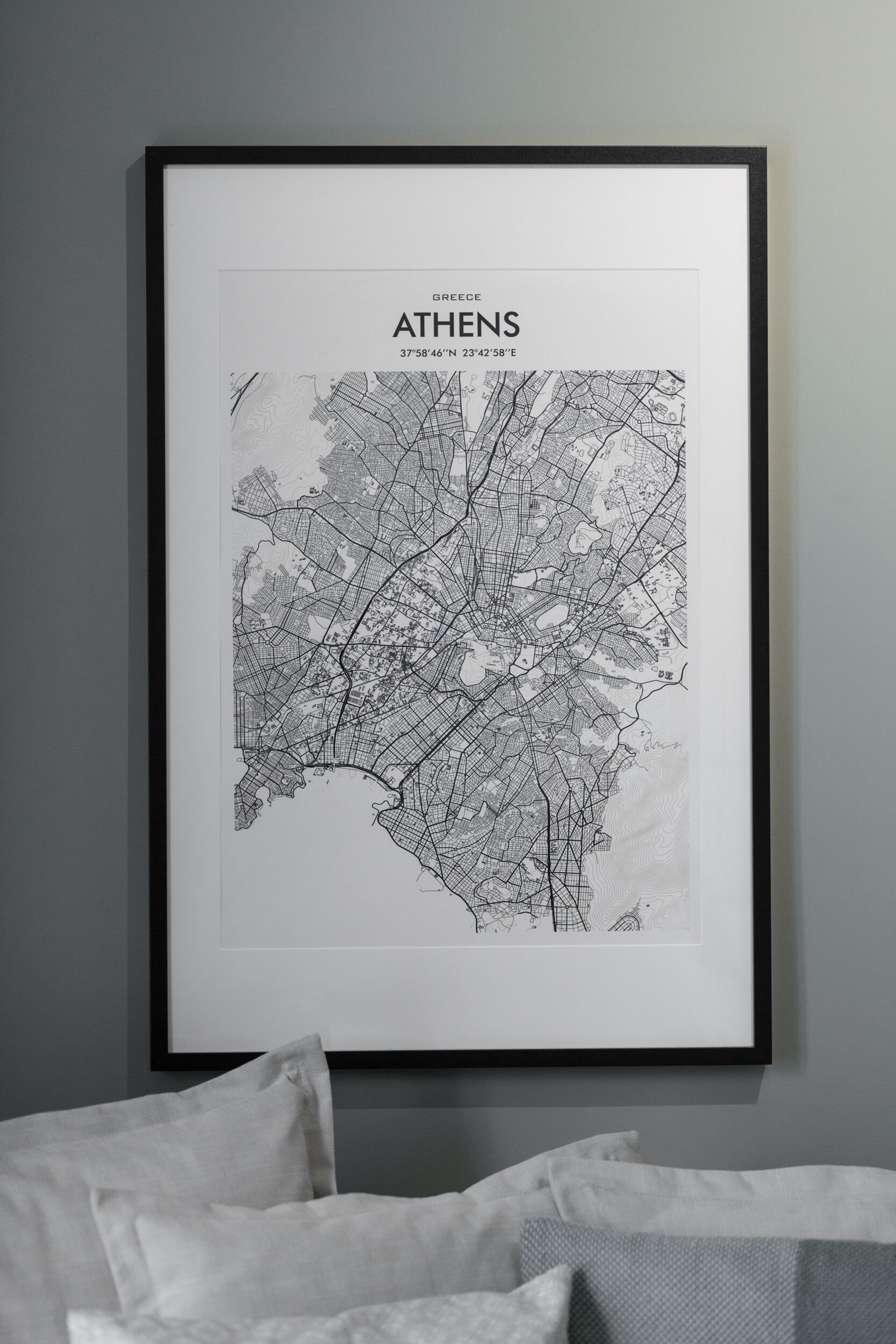 A framed map of Athens, Greece, with a black frame and white bedding in the foreground.