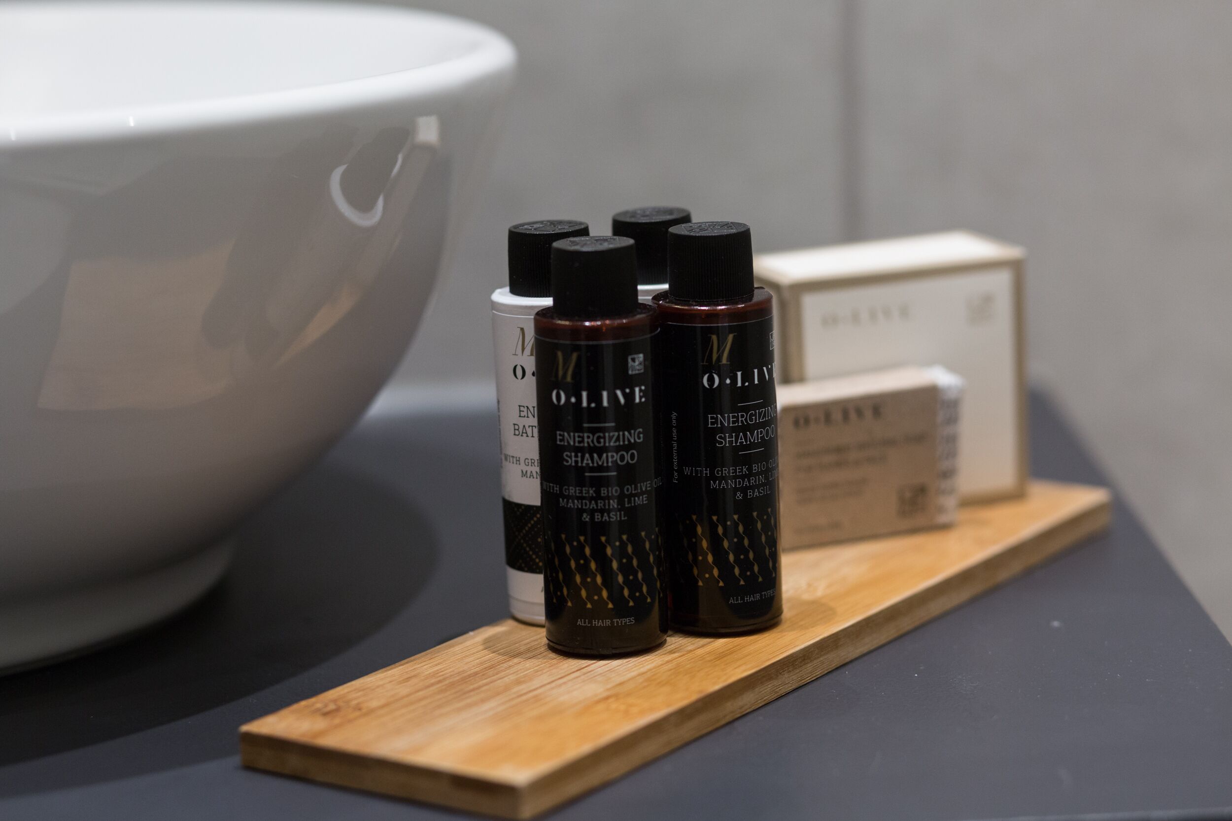 A wooden tray with three bottles of Energizing Shampoo and a white box on a dark surface.