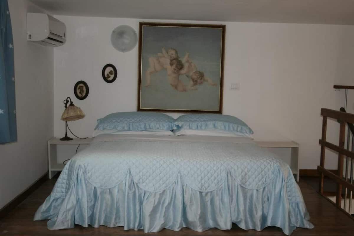Ein Schlafzimmer mit einem Bett, einer Wandklimaanlage, einem gerahmten Gemälde und einem Nachttisch mit Lampe.