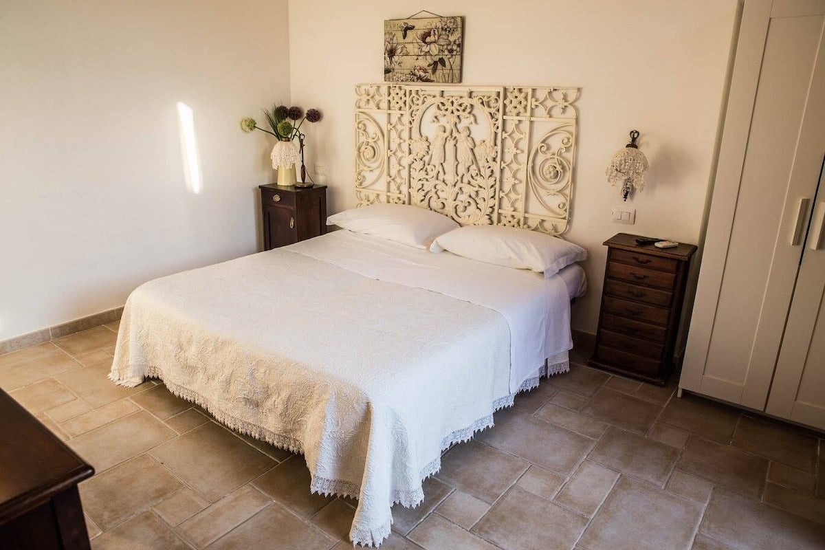 Ein Schlafzimmer mit einem großen Bett, einem Nachttisch, einer Kommode und einem dekorativen Kopfteil.