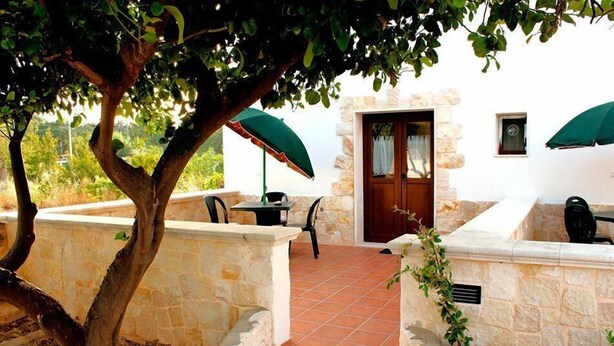 A stone-walled outdoor patio with a table and chairs, a door, and a green umbrella. - Alba e tramonto B&B (Mola di Bari)