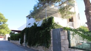 A white two-story building with a stone wall and a metal fence. - Beach Apartment Jakobus (Lumbarda)