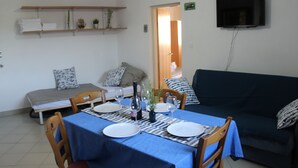 A dining area with a table set for two, a sofa, and a TV mounted on the wall. - Beach Apartment Jakobus (Lumbarda)