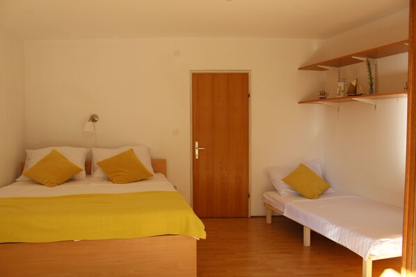 A bedroom with a bed, a bedside table, a chair, a door, and a shelf with items.
