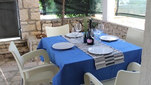 A table set for two with a blue tablecloth, white chairs, and a stone wall in the background. - Beach Apartment Jakobus (Lumbarda)