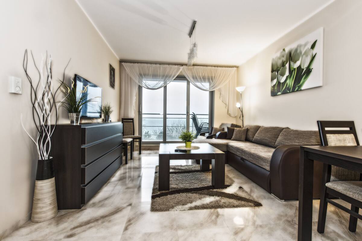 Una sala de estar moderna con un sofá, una mesa de centro y vistas al exterior a través de amplios ventanales.