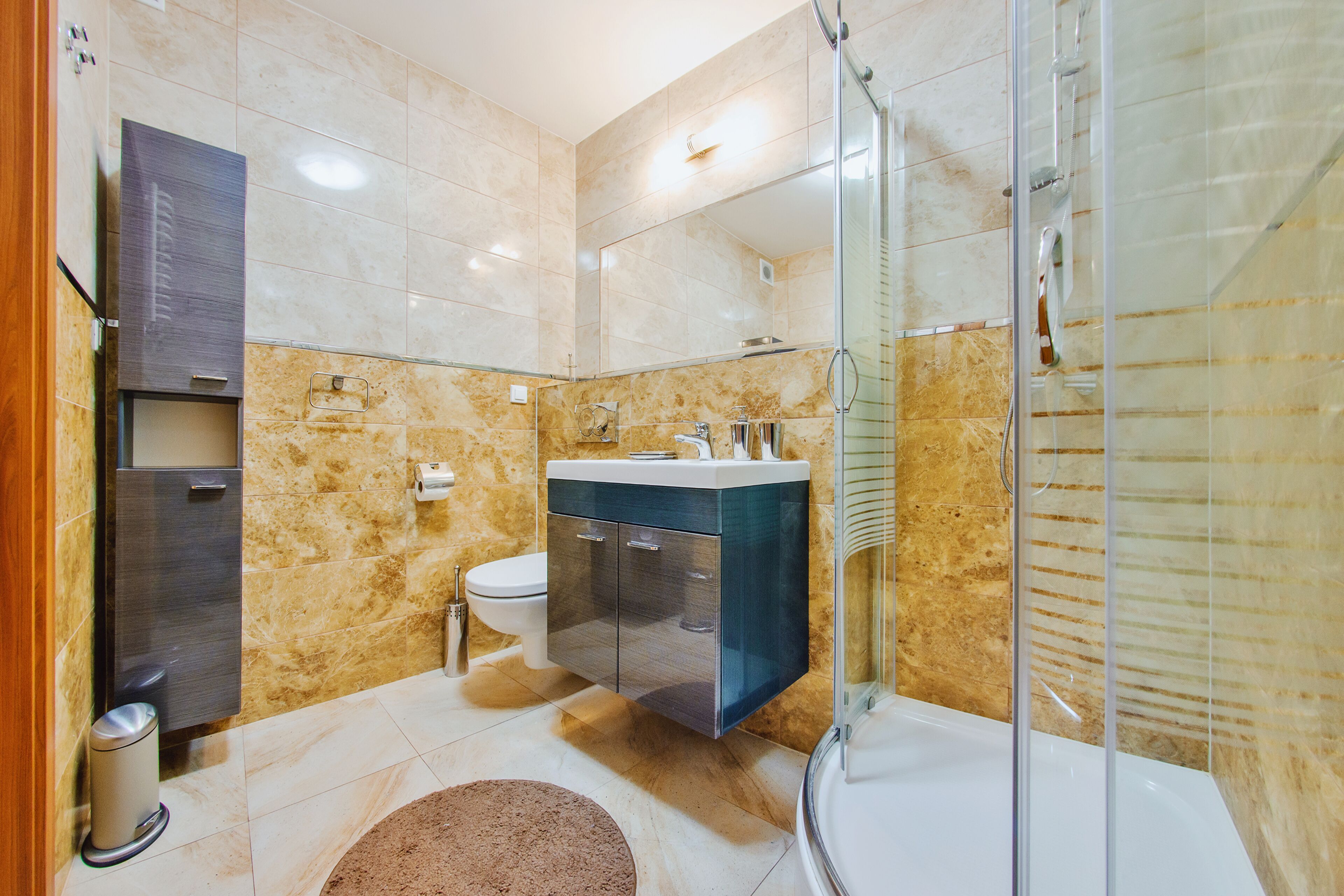 A modern bathroom with a glass-enclosed shower, a marble-tiled wall, a built-in sink, and a toilet.