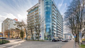 A modern multi-story building with a curved glass facade, surrounded by trees and parked cars. - Sun & Snow Wechta - Promenada Gwiazd (Miedzyzdroje)