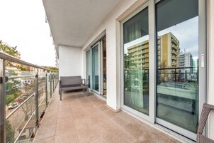 A balcony with a bench, large glass doors, and a view of a cityscape.