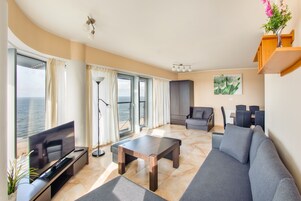A modern living room with a flat-screen TV, a wooden coffee table, a gray sofa, and a dining area with chairs.