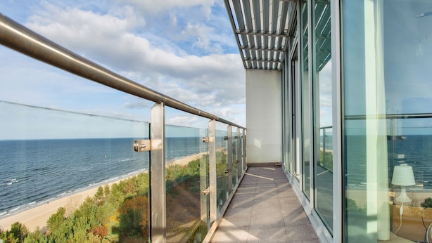 A balcony with a glass railing overlooking a beach and the sea. - Sun & Snow Wechta - Promenada Gwiazd (Miedzyzdroje)