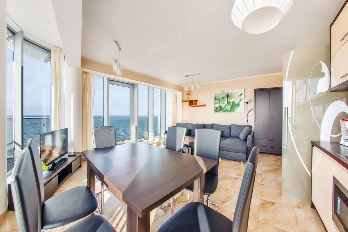 Una sala de estar moderna con comedor, ventanas amplias y vista al mar.