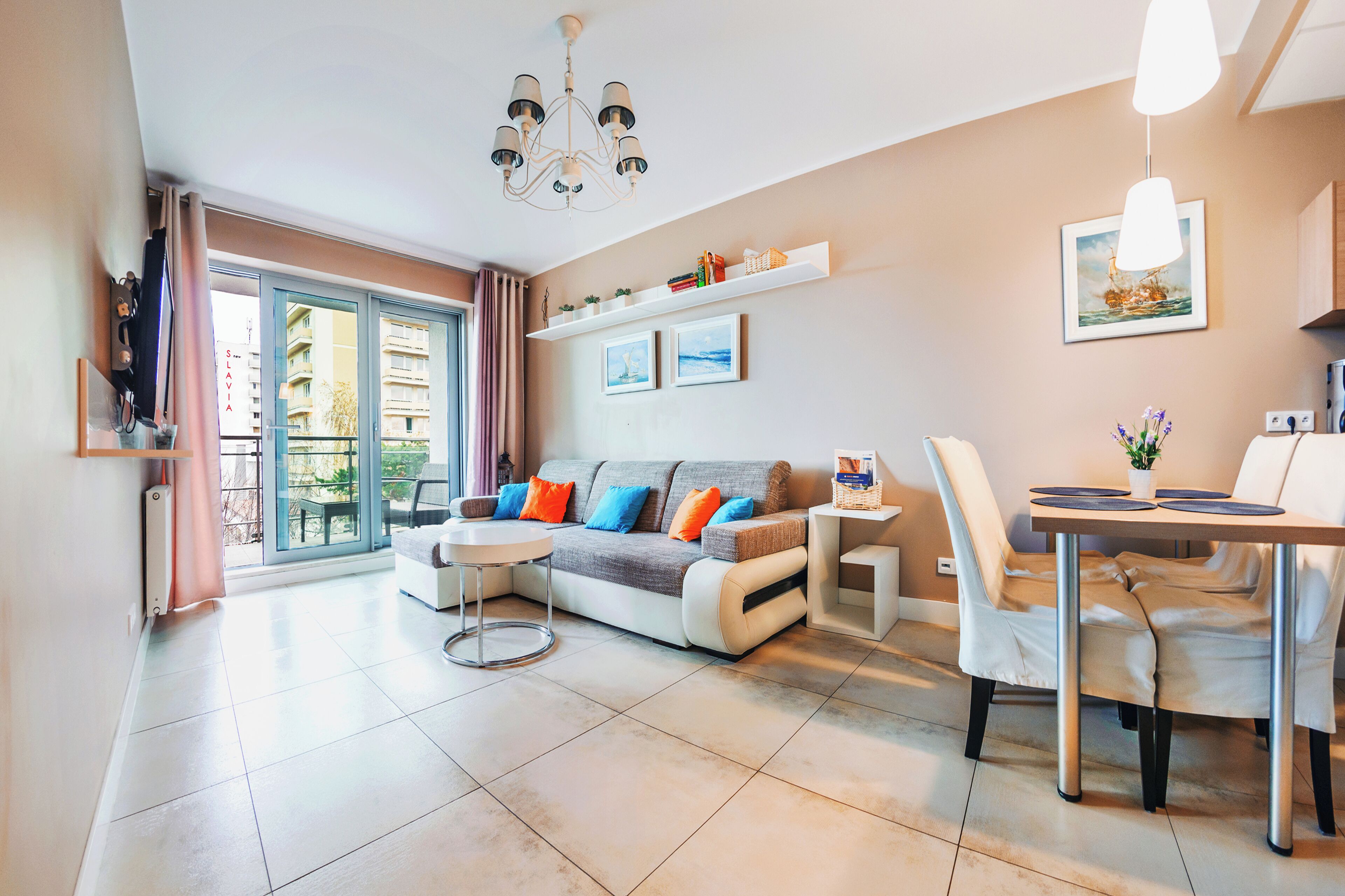 Ein modernes Wohnzimmer mit Sofa, Couchtisch, Esstisch und Stühlen. Eine Chandelier, ein Fenster mit Vorhängen und ein Wandregal mit Bildern sind ebenfalls vorhanden.