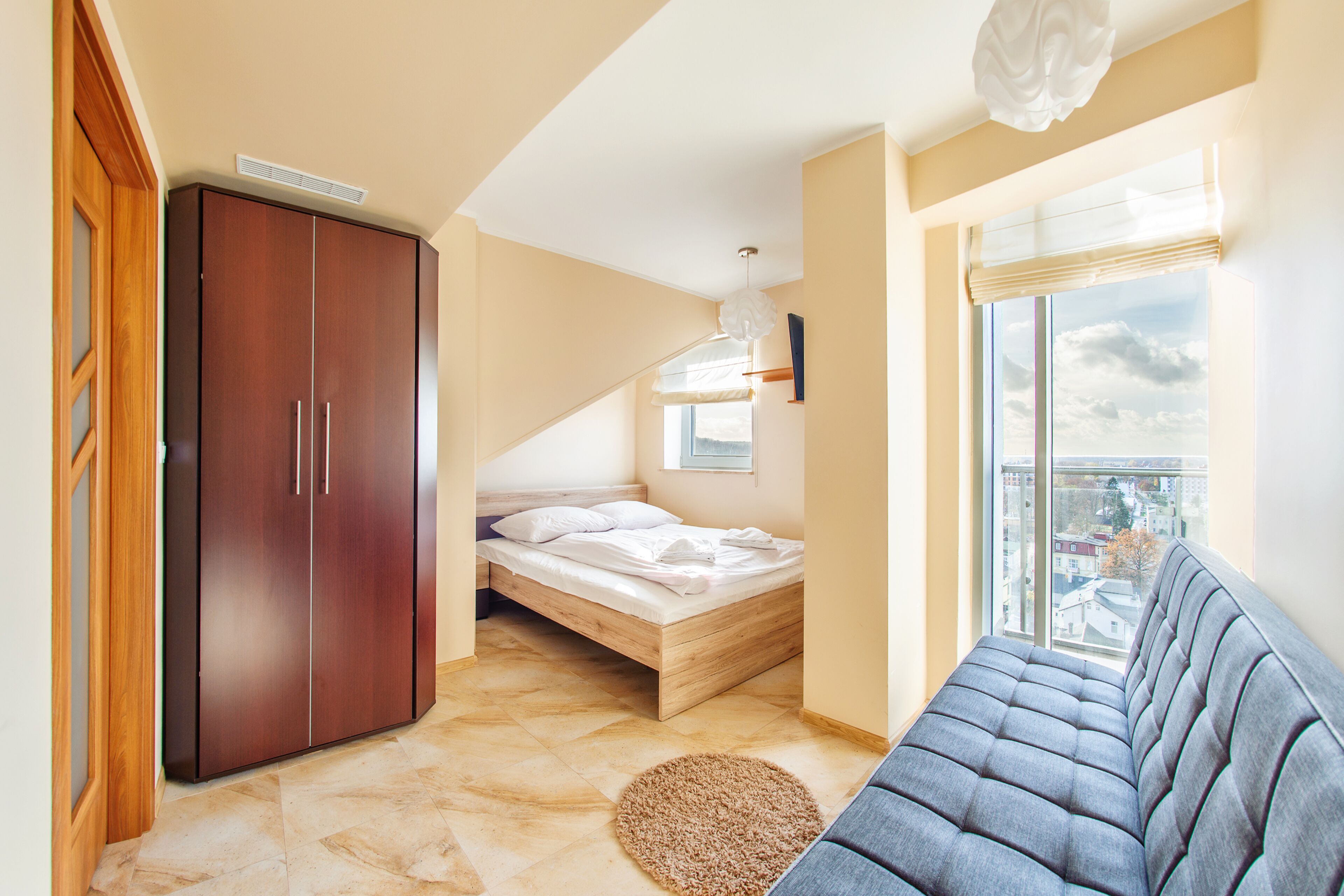 A bedroom with a bed, wardrobe, and a view of the city through a window.
